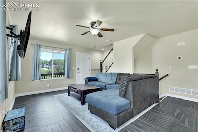 Living room with a ceiling fan, stairs, and dark wood-style flooring