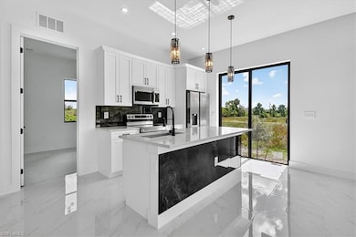 Kitchen featuring light stone countertops, white cabinets, backsplash, stainless steel appliances, and an island with sink