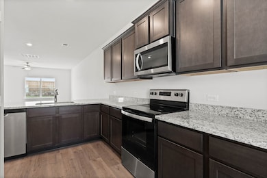 Kitchen featuring appliances with stainless steel finishes, dark brown cabinetry, light wood-type flooring, light stone countertops, and recessed lighting