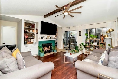 Living room with dark wood-style flooring, a fireplace with flush hearth, a ceiling fan, and built in features