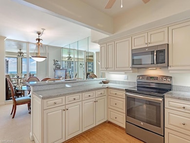 Kitchen with cream cabinets, ceiling fan, appliances with stainless steel finishes, light stone counters, and a peninsula