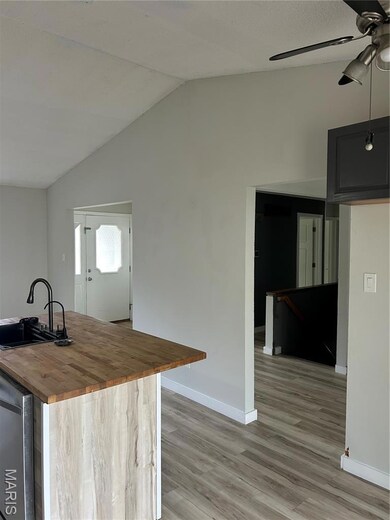 Kitchen featuring butcher block counters, a ceiling fan, light wood-type flooring, lofted ceiling, and a center island with sink