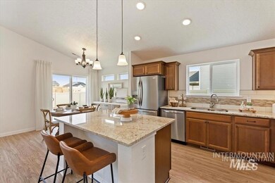 Kitchen featuring stainless steel appliances, brown cabinetry, a center island, a chandelier, and lofted ceiling