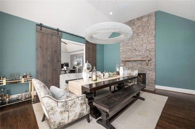 Dining space with a stone fireplace, dark wood finished floors, a barn door, and high vaulted ceiling
