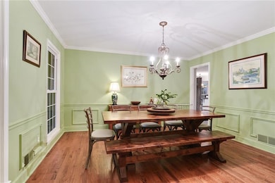 Dining space featuring wood finished floors, a decorative wall, a chandelier, crown molding, and a wainscoted wall