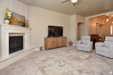 Carpeted living room featuring arched walkways, a ceiling fan, a glass covered fireplace, and a barn door