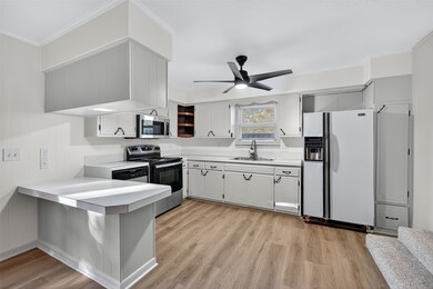 Kitchen with a peninsula, stainless steel appliances, light countertops, light wood-style flooring, and ornamental molding