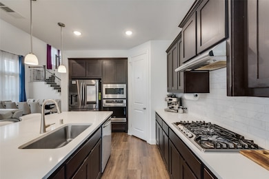 Kitchen featuring dark brown cabinets, stainless steel appliances, light wood-type flooring, pendant lighting, and recessed lighting