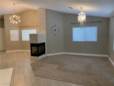 Unfurnished living room featuring a chandelier, a stone fireplace, wood tiled floors, and high vaulted ceiling