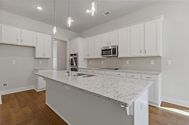 Kitchen featuring white cabinetry, decorative backsplash, decorative light fixtures, light stone countertops, and dark wood-style flooring