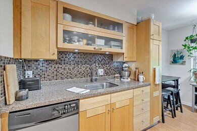 Kitchen featuring stainless steel dishwasher, light brown cabinets, backsplash, light wood-type flooring, and glass insert cabinets