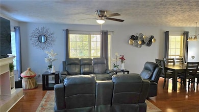 Living area with wood finished floors, a textured ceiling, ceiling fan, and a fireplace with raised hearth