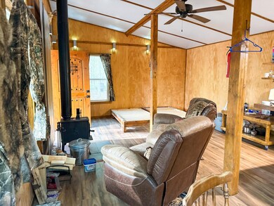 Living room with vaulted ceiling, wood finished floors, wooden walls, a wood stove, and ceiling fan
