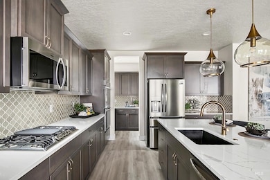 Kitchen featuring light wood-style flooring, stainless steel appliances, decorative light fixtures, backsplash, and a textured ceiling