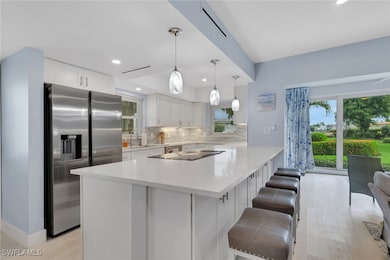 Kitchen featuring white cabinetry, stainless steel fridge with ice dispenser, backsplash, pendant lighting, and a breakfast bar
