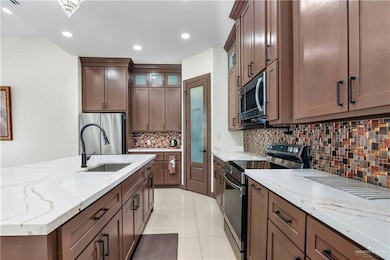 Kitchen with appliances with stainless steel finishes, light stone countertops, backsplash, glass insert cabinets, and light tile patterned flooring