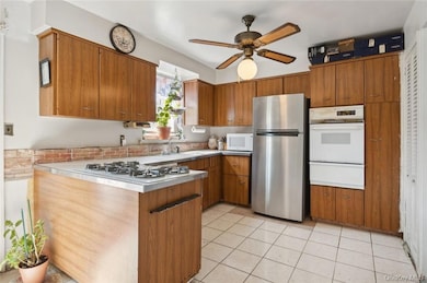 Kitchen featuring white appliances, sink, ceiling fan, and light tile floors