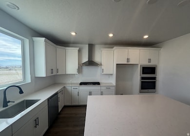 Kitchen with wall chimney exhaust hood, stainless steel appliances, white cabinets, recessed lighting, and dark wood-type flooring