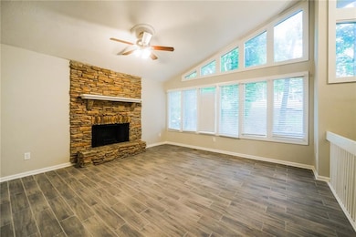 Unfurnished living room featuring ceiling fan, healthy amount of natural light, a stone fireplace, dark wood-type flooring, and high vaulted ceiling