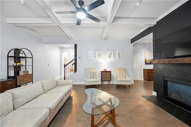 Living area featuring coffered ceiling, hardwood / wood-style floors, a ceiling fan, stairs, and a brick fireplace