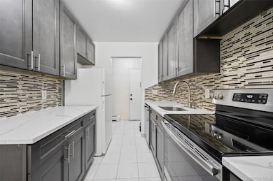 Kitchen featuring stainless steel appliances, light tile patterned floors, light stone counters, tasteful backsplash, and baseboard heating