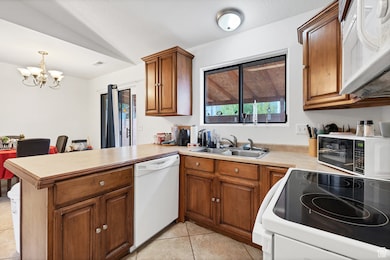 Kitchen with white appliances, a peninsula, brown cabinets, a chandelier, and light countertops