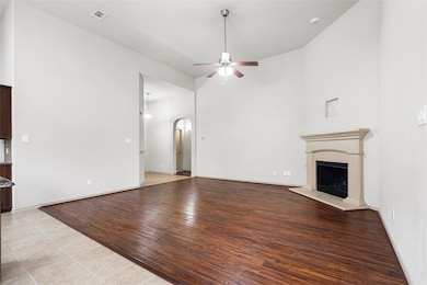 Unfurnished living room with high vaulted ceiling, light wood-style flooring, arched walkways, a fireplace with raised hearth, and ceiling fan