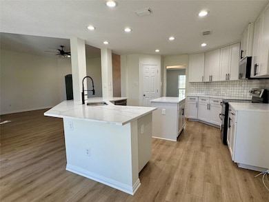 Kitchen featuring recessed lighting, stainless steel appliances, backsplash, white cabinets, and light wood finished floors