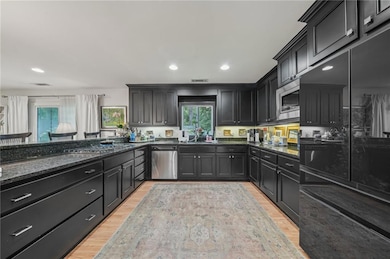 The remodeled, updated kitchen features stainless steel and black appliances, light wood finished floors, dark stone countertops, dark cabinetry, and recessed lighting