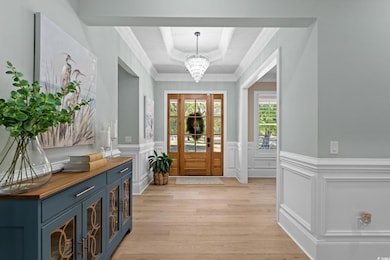 Foyer entrance with a notable chandelier, light wood-style floors, wainscoting, a raised ceiling, and a decorative wall