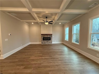 Unfurnished living room featuring beamed ceiling, coffered ceiling, dark wood-type flooring, a fireplace, and a ceiling fan