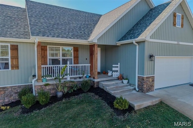 Doorway to property featuring a shingled roof, covered porch, concrete driveway, stone siding, and a garage