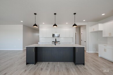 Kitchen featuring decorative backsplash, white cabinets, a center island with sink, pendant lighting, and light wood-type flooring