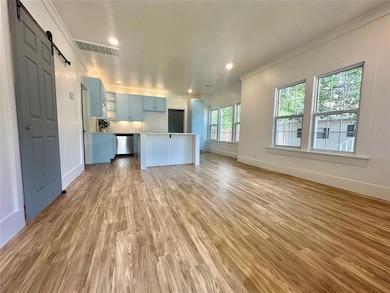 Unfurnished living room with a barn door, ornamental molding, light wood finished floors, baseboards, and recessed lighting