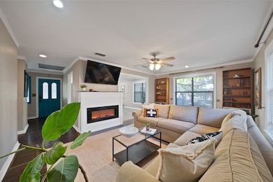 Living room with ornamental molding, wood finished floors, a glass covered fireplace, recessed lighting, and ceiling fan