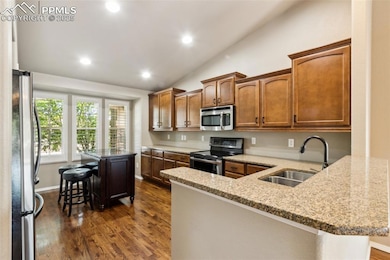 Kitchen with stainless steel appliacne, a sink, dark wood finished floors, vaulted ceiling, and an island