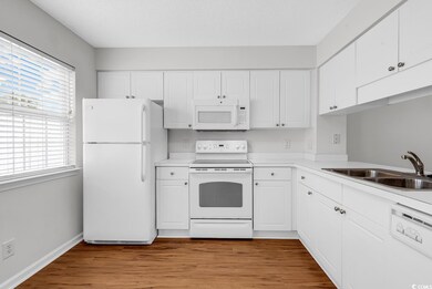 Kitchen with a sink, white appliances, plenty of natural light, and white cabinets