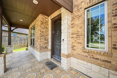This photo showcases a welcoming front porch with a brick and stone exterior, featuring decorative patterned tile flooring, recessed lighting, and large windows that offer ample natural light.