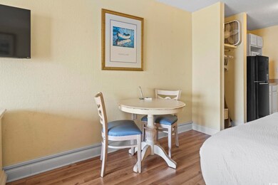 Bedroom with freestanding refrigerator, wood finished floors, and baseboards
