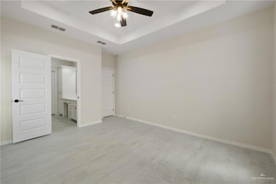 Unfurnished bedroom featuring a raised ceiling, light wood-style floors, baseboards, and connected bathroom