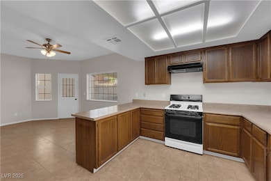 Kitchen featuring range with gas stovetop, a peninsula, light countertops, a ceiling fan, and open floor plan