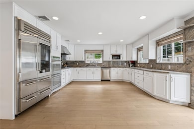 Kitchen with built in appliances, white cabinets, backsplash, light wood-style flooring, and recessed lighting