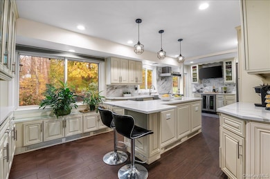Kitchen featuring cream cabinetry, glass insert cabinets, pendant lighting, light stone counters, and recessed lighting