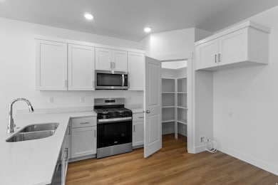 Kitchen with stainless steel appliances, light wood-type flooring, white cabinetry, light stone countertops, and recessed lighting