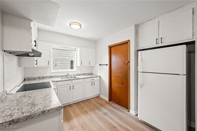 Kitchen with light hardwood / wood-style floors, sink, range, white cabinets, and white fridge