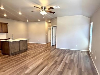 Kitchen featuring open floor plan, ceiling fan, light countertops, wood finished floors, and a kitchen island with sink