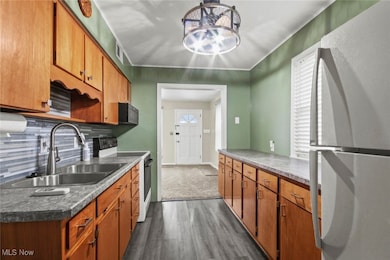 Kitchen featuring white appliances, brown cabinetry, dark wood finished floors, crown molding, and backsplash