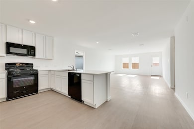 Kitchen featuring black appliances, white cabinetry, a peninsula, light wood-style floors, and open floor plan
