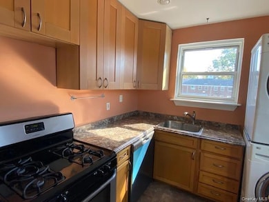 Kitchen featuring stainless steel appliances, stacked washer / drying machine, dark stone countertops, and dark tile patterned floors