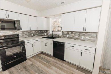 Kitchen featuring black appliances, a textured ceiling, white cabinets, light wood-type flooring, and ornamental molding